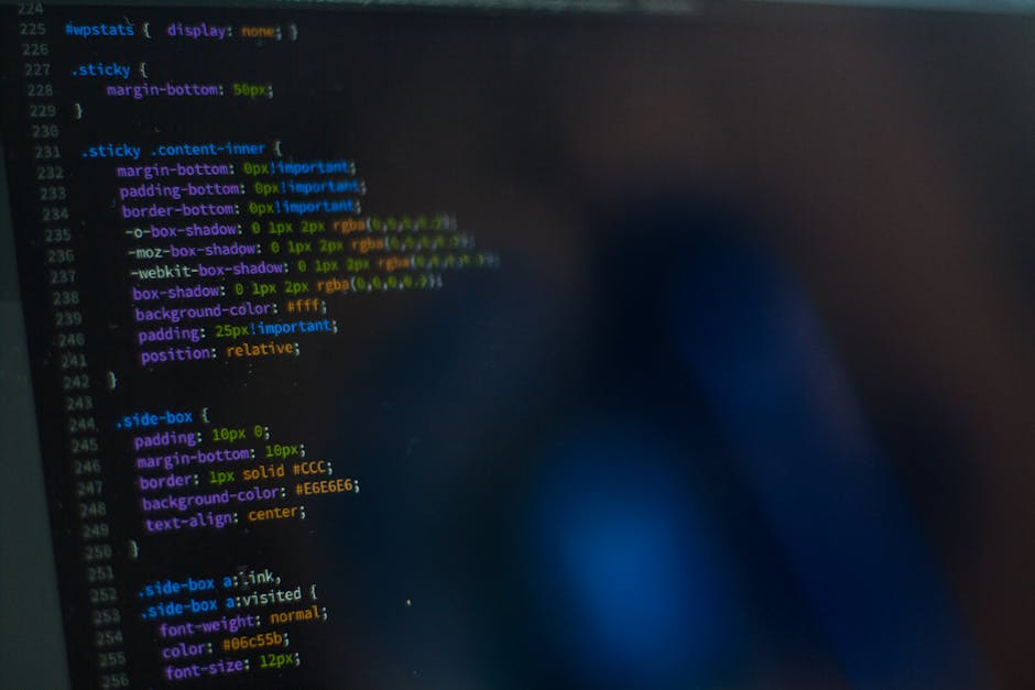 A close-up view of a laptop displaying lines of colorful programming code on its screen, placed on a wooden desk. Next to the laptop is a ceramic coffee mug with the phrase 'This coffee is making me a